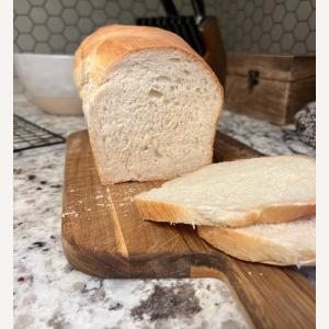 Sliced loaf of homemade sourdough sandwich bread on a wooden cutting board in a home kitchen.